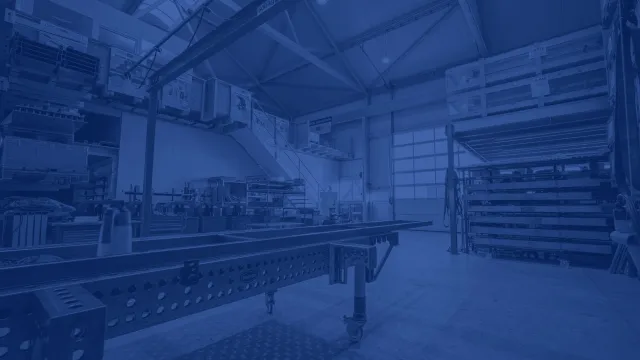 Produktionshalle von CREAMETAL mit langem Montagetisch, Kranbahn und beschrifteten Transportkisten in den Regalen